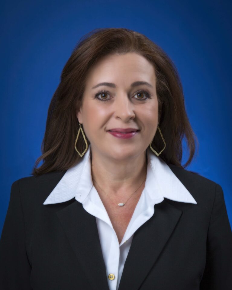 Finished headshot of a smiling woman in a black jacket and white collar on a blue backdrop