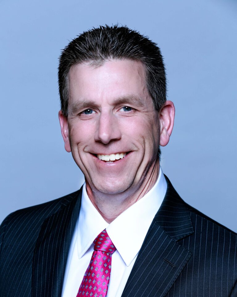 Finished headshot of a smiling man in a pinstripe suit and pink tie on a blue backdrop