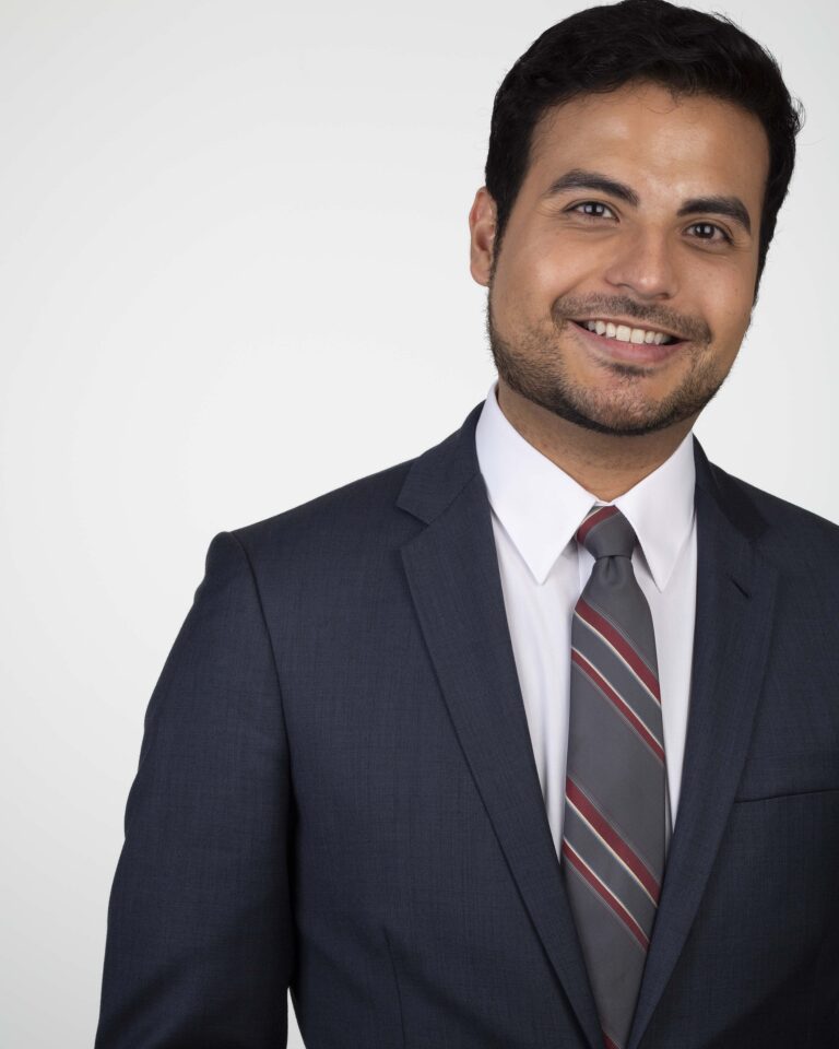 Finished headshot of a smiling man in a navy suit and striped tie on a white backdrop