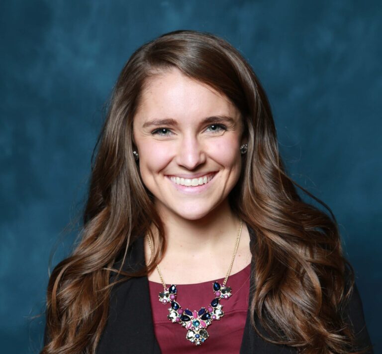 Finished headshot of a smiling woman in a burgundy top and necklace on a blue backdrop