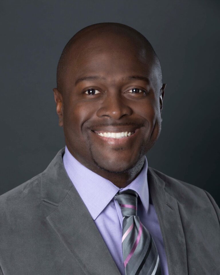 Finished headshot of a smiling man in a gray suit and lavender shirt on a dark gray backdrop