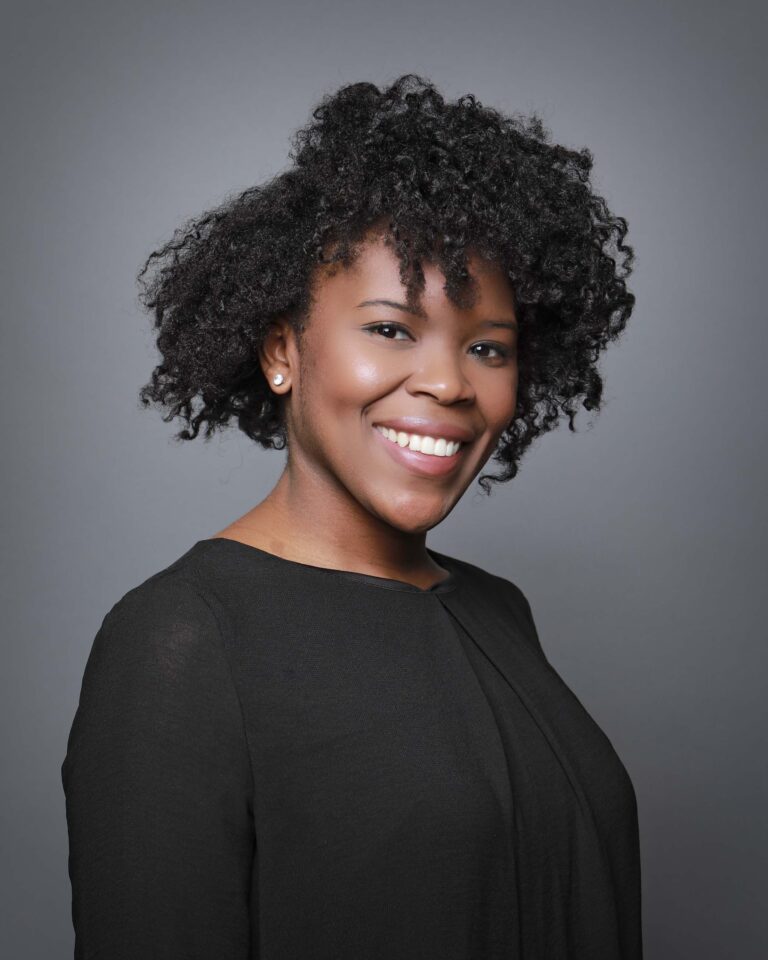 Finished headshot of a smiling woman with curly hair in a black top on a gray backdrop