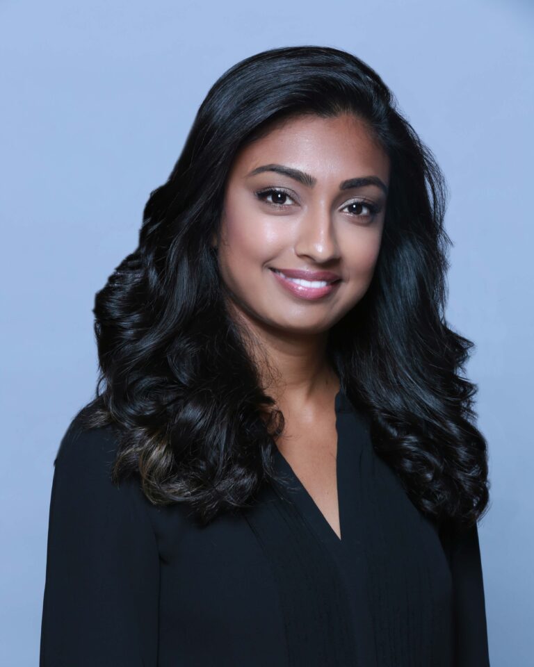 Finished headshot of a smiling woman with long dark hair in a black blouse on a light blue backdrop