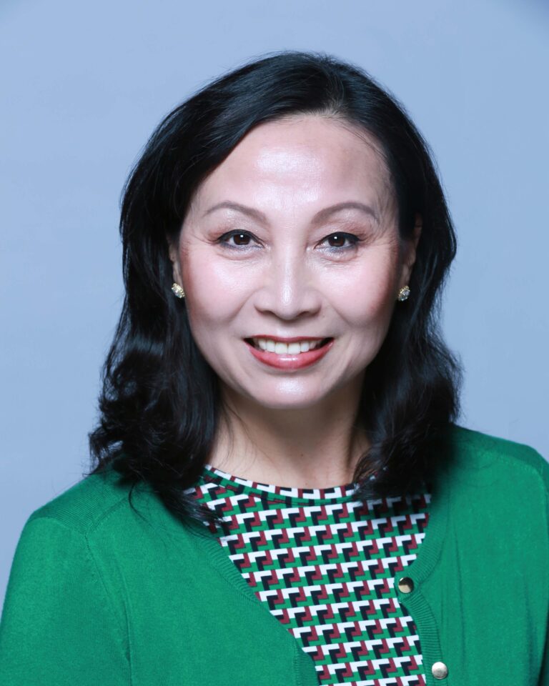 Finished headshot of a smiling woman in a green cardigan on a light blue backdrop