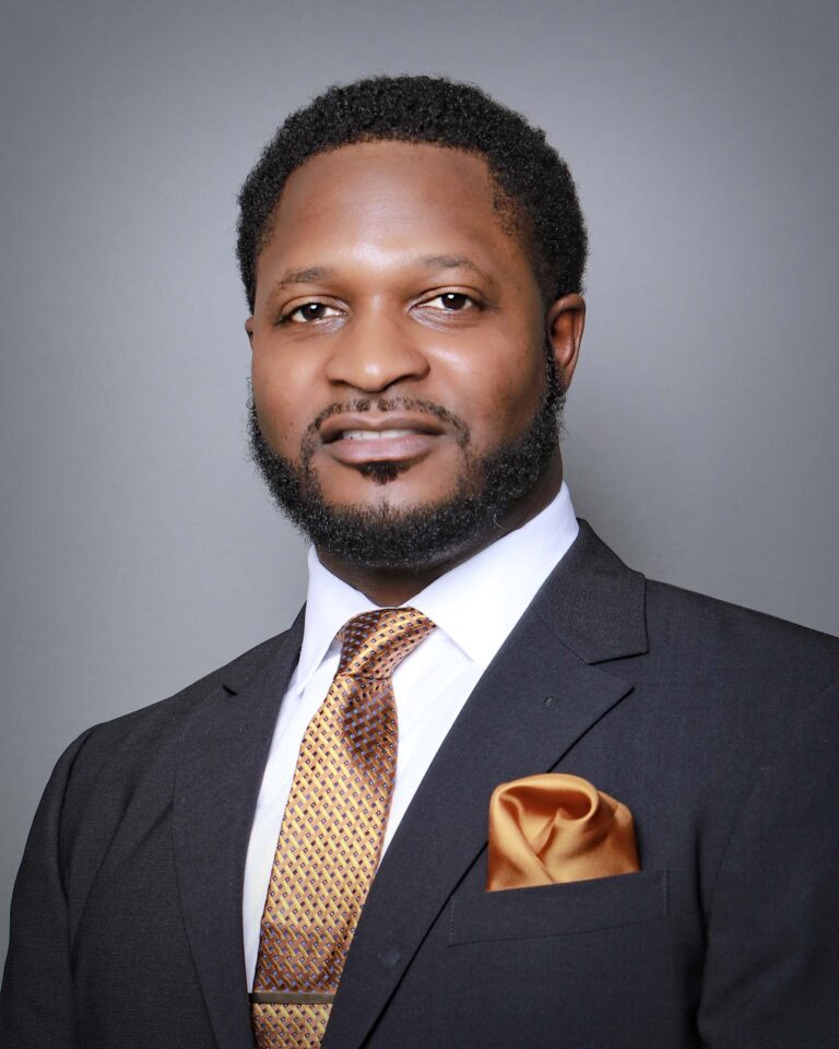 Finished headshot of a smiling man in a charcoal suit, gold tie and pocket square on a gray backdrop