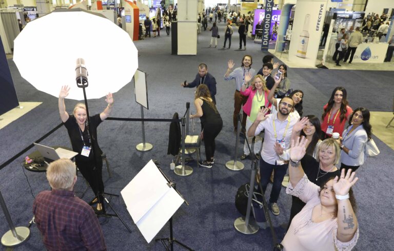 Attendees waving from the line at a headshot lounge on the Gaylord National Harbor convention floor