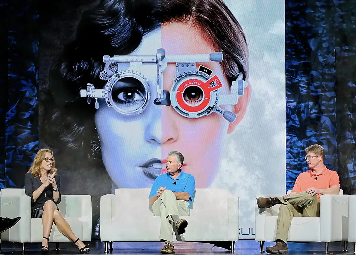 Orlando, Florida convention photography of a vision care conference panel on stage at the Gaylord Palms, with a large phoropter graphic on the screen behind the three seated speakers.