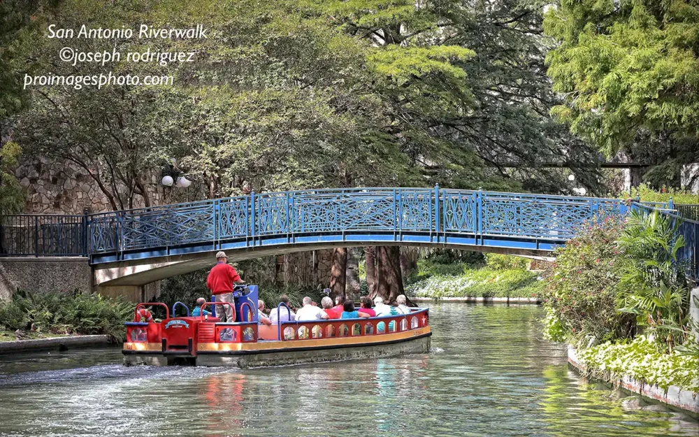 A San Antonio River Walk cruise boat gracefully floating down the picturesque river, surrounded by vibrant spring blooms and the lively charm of the city.