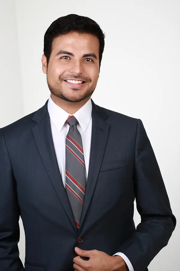 Finished headshot of a smiling man in a dark suit, white shirt and striped tie on a light backdrop