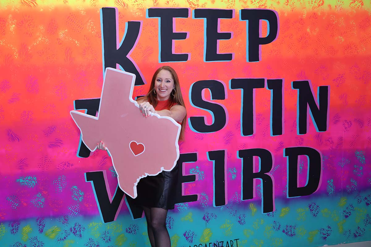 Austin, Texas corporate event photography of an attendee holding a Texas prop at a Keep Austin Weird mural backdrop.