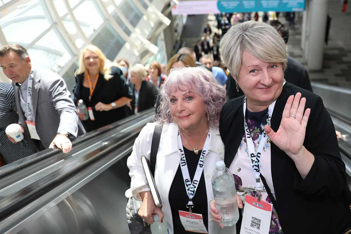 San Diego corporate conference photography capturing two smiling attendees waving on a convention center escalator.